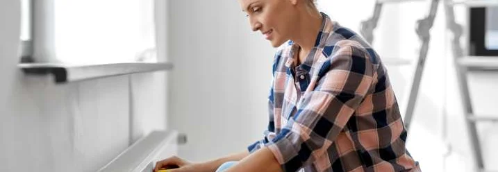 Eine Person misst einen Heizkörper mit einem Maßband aus.